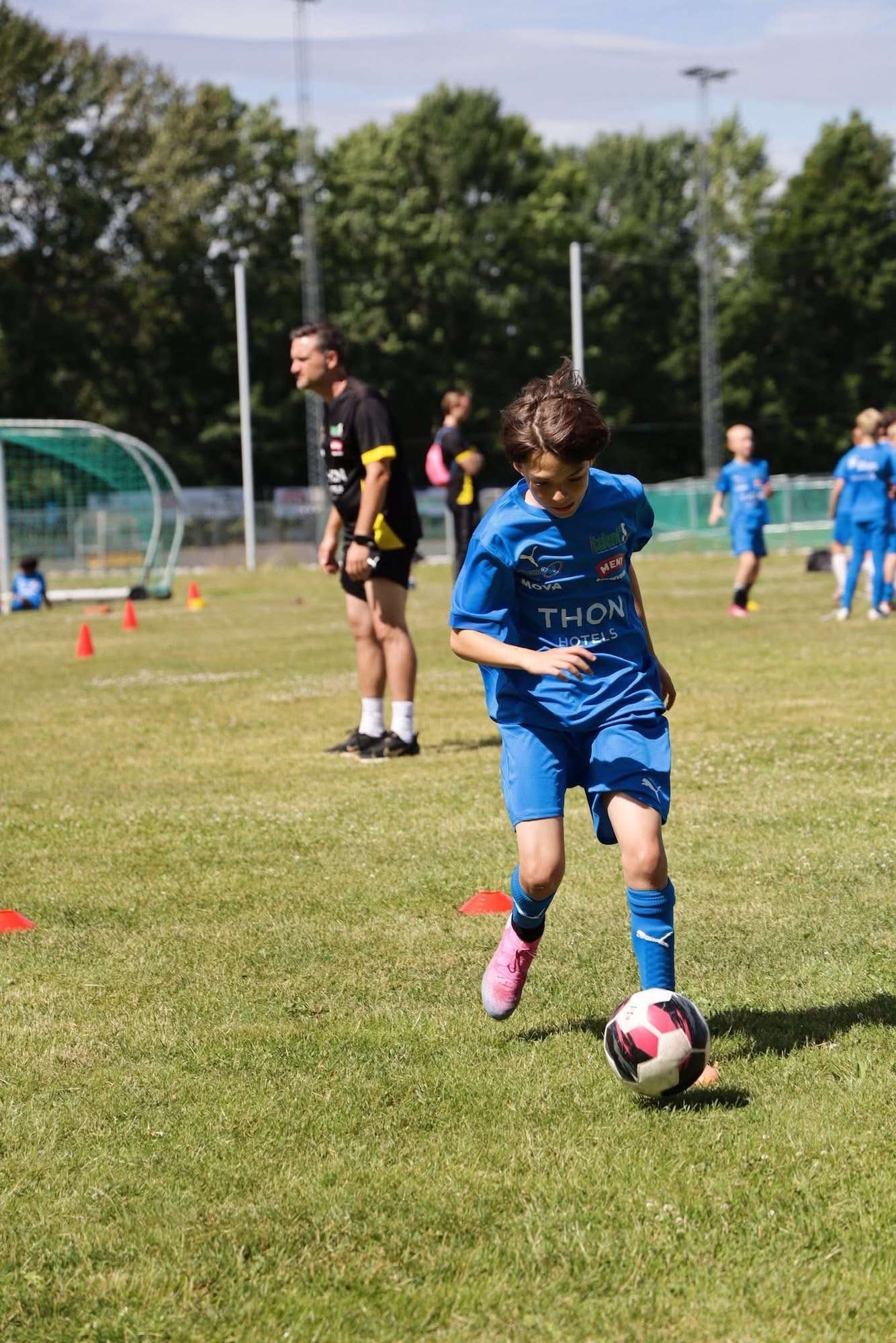 Spiller i blå Italent-drakt fører ballen på gresset under fotballskolen